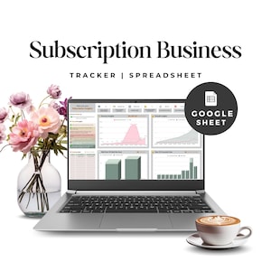 May include: A silver laptop displaying a Subscription Business Tracker spreadsheet with data charts and graphs. The screen shows revenue and growth insights. A clear glass vase with pink flowers and a white coffee cup sit beside the laptop.