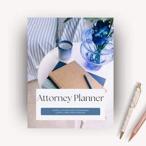 May include: An Attorney Planner with a tan cover, a blue pen, and a white label featuring the text Attorney Planner and Your all-in-one guide for managing clients, cases, and schedules. The planner sits on a white table with a blue glass vase.