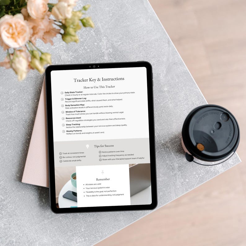 An iPad displaying a Tracker Key  Instructions sheet on a table, with tips for success and a reminder about mindfulness. A coffee cup is beside it, and there are soft blooms in the background.
