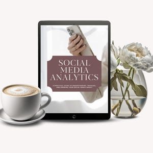 Pode incluir: Um tablet digital exibe a capa de um livro intitulado "Social Media Analytics". Uma xícara de café com arte latte está em um pires à esquerda. Um vaso de flores brancas está à direita. Uma mão segurando um telefone é visível.