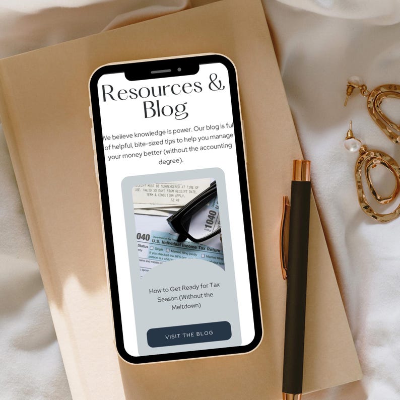 A mobile phone displaying a finance blog titled 'Resources  Blog' with a focus on tax tips, set on a beige surface next to a black pen and gold jewelry.