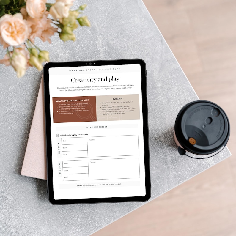 An iPad displaying a weekly planner page titled 'Creativity and Play' with guidance and mini-exercises. A coffee cup and flowers are in the foreground, on a light-colored table.