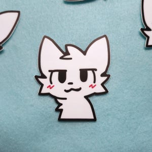 May include: White sticker of a cartoon cat with black eyes and red blush on its cheeks. The cat has a surprised expression.