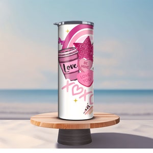 Può includere: Un bicchiere termico in acciaio inossidabile bianco con un design rosa e bianco che presenta una tazza di caffè, una stella, un arcobaleno e cuori con il testo "Love", "Be Mine" e "Love You".