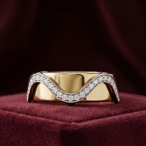 Peut inclure: Une bague en or avec un motif ondulé ornée de petits diamants étincelants. La bague est présentée sur un fond de velours rouge foncé, soulignant son aspect luxueux. La bande est de couleur or massif.
