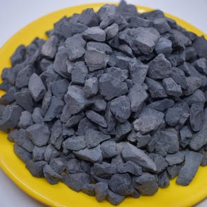 Può includere: Un piatto giallo pieno di piccole pietre di colore grigio scuro di forma irregolare.