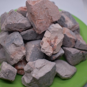 May include: A pile of light grey and pink clay rocks on a green plate. The rocks are irregular in shape and have a rough texture.