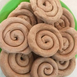 May include: A close-up of a plate of brown, spiral-shaped biscuits. The biscuits are arranged in a pile, and they are all the same size and shape.