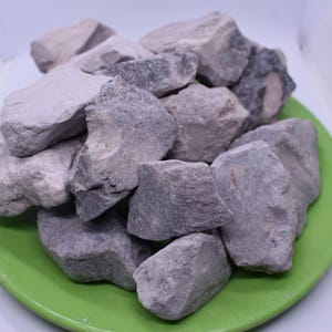 May include: A pile of gray and purple clay rocks on a green plate. The rocks are irregular in shape and have a rough texture.