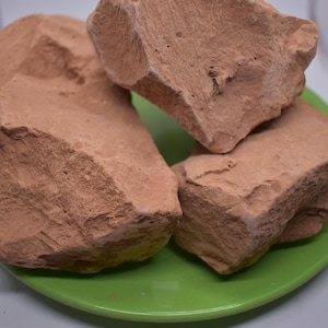 Könnte beinhalten: Vier große, unregelmäßig geformte Stücke brauner Tonerde auf einem grünen Teller. Die Tonerde hat eine raue, strukturierte Oberfläche.