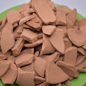 May include: A close-up of a pile of terracotta shards on a green plate. The shards are of various sizes and shapes, and they are all a reddish-brown colour.