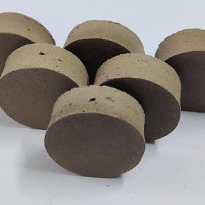 May include: Six brown cork stoppers with dark brown bases are arranged in a group. Each stopper has a cylindrical shape with a flat top and bottom. The stoppers are slightly overlapping.