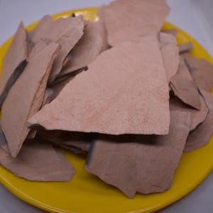 May include: A pile of light brown, irregularly shaped clay pieces on a yellow plate.