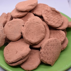 May include: A pile of round, brown clay discs on a green plate. The discs are all about the same size and have a rough, textured surface.