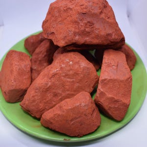 May include: A pile of red clay rocks on a green plate. The rocks are irregular in shape and have a rough texture.