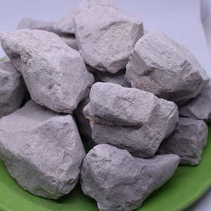 Könnte beinhalten: Ein Haufen hellgrauer, unregelmäßig geformter Steine, möglicherweise Ton, liegt auf einem leuchtend grünen Teller. Die Steine haben eine raue, strukturierte Oberfläche und variieren in der Größe.