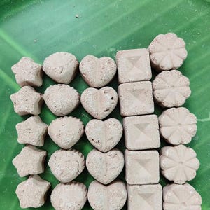 Puede incluir: Una variedad de formas texturizadas de color marrón claro, que incluyen estrellas, formas redondas, corazones, cuadrados y formas de flores. Los objetos están dispuestos sobre una superficie verde.
