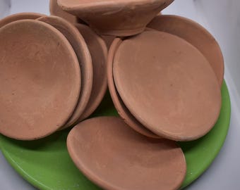Puede incluir: Un conjunto de seis cuencos de terracota, todos con una forma y tamaño similares, están dispuestos sobre una superficie verde. Los cuencos están hechos de arcilla marrón rojiza y tienen un acabado liso y ligeramente texturizado.