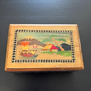 May include: A white ceramic mug with a black handle and the text "But First, Coffee" in a bold, black font. The mug is set against a blurred background, suggesting a cozy setting.