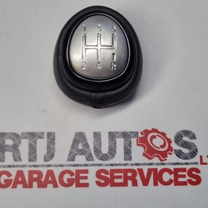 May include: A black leather gear shift knob with a silver top. The top has a 5-speed gear pattern with the numbers 1, 2, 3, 4, 5, and R.