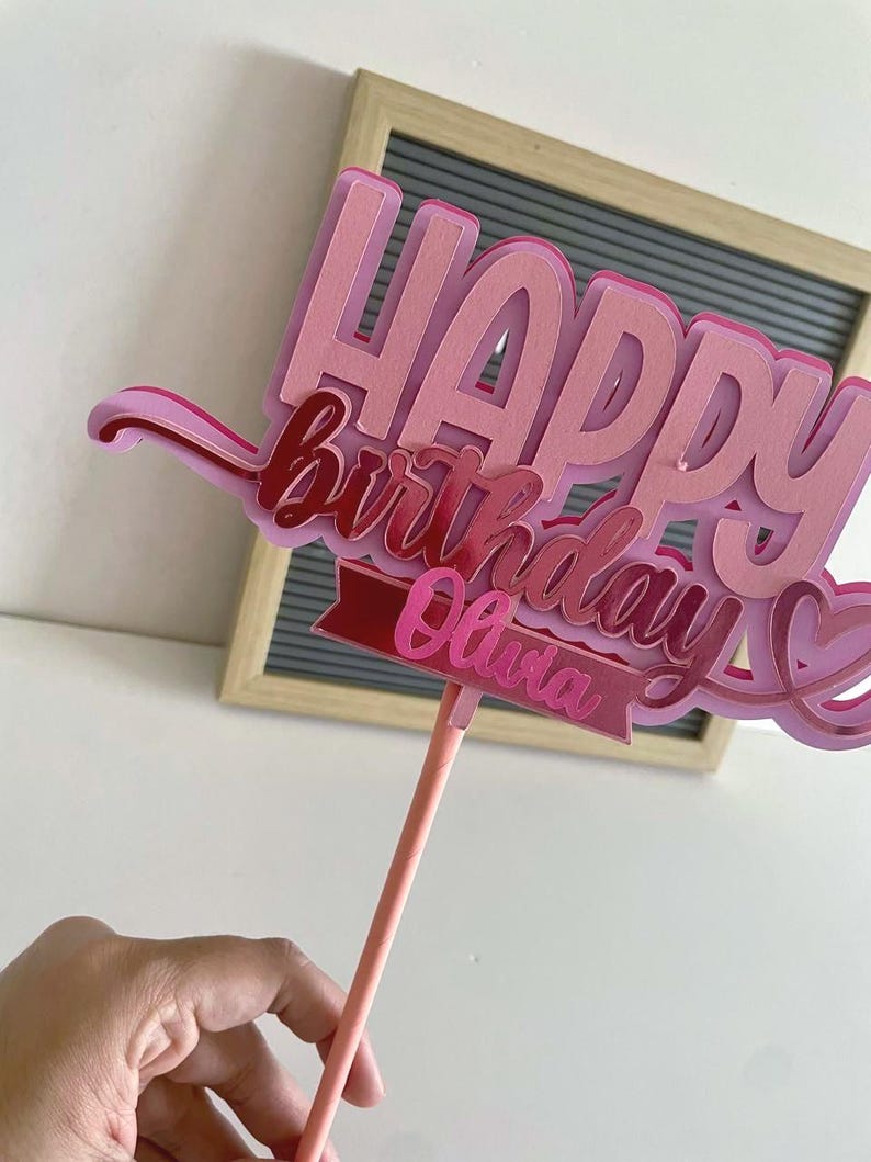 Side view of the pink layered cardstock Happy Birthday cake topper showing paper layers and dimensional depth on a stick.