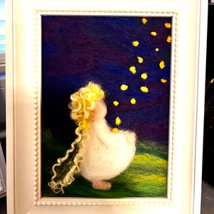 Puede incluir: Una obra de arte de fieltro de aguja enmarcada que representa una pequeña figura blanca de hada con cabello rubio, sentada en un campo verde y mirando hacia arriba a un cielo nocturno azul oscuro con estrellas amarillas.