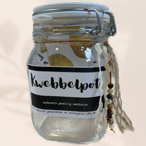 Könnte beinhalten: Ein Glasgefäß mit einem weißen Deckel und einem schwarzen Etikett, auf dem "Kwebbelpot" steht, sowie dem Text "ouderwets gezellig kwebbelen" und "voor lachbuien gesprekken en onvergetelijke momenten". Das Gefäß ist mit kleinen Papierstücken gefüllt und hat eine braune und weiße Schnur mit Perlen, die vom Deckel hängen.