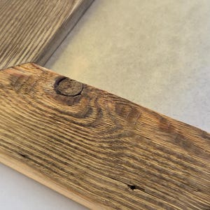 May include: A rectangular picture frame constructed from natural wood with a prominent grain pattern and a visible knot in the corner. The frame features mitered joints and a light-colored inner border surrounding a plain, light-toned center panel.
