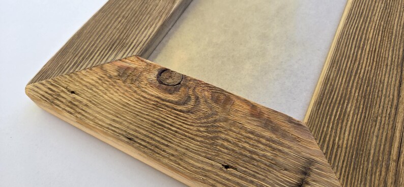 May include: A rectangular picture frame constructed from natural wood with a prominent grain pattern and a visible knot in the corner. The frame features mitered joints and a light-colored inner border surrounding a plain, light-toned center panel.