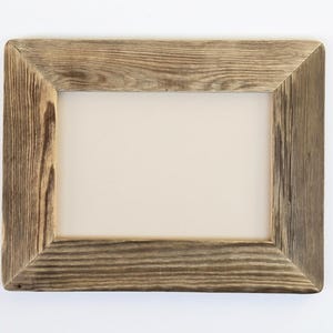 May include: A rectangular picture frame constructed from weathered brown wood with a visible grain pattern. The frame features mitered corners and a plain, light beige rectangular insert centered within the opening of the wooden border.