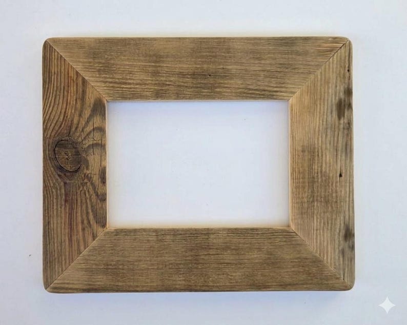 May include: A rectangular picture frame constructed from weathered brown wood with a visible grain pattern and a prominent knot on the left side. The frame features mitered corners and a wide, flat border surrounding a central rectangular opening.
