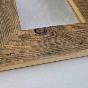 May include: A rectangular picture frame constructed from weathered, reclaimed wood with a prominent natural grain pattern. The frame features mitered corners and a visible knot in the wood on the bottom rail, showcasing a rustic, textured surface.