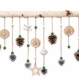 May include: A wall hanging decoration featuring a horizontal birch branch suspended by twine. Hanging from the branch are various ornaments including natural pinecones, white-tipped pinecones, wooden star cutouts, and small white and green beads.