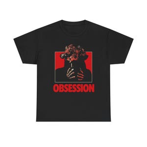 Könnte beinhalten: Ein schwarzes Kurzarm-T-Shirt mit einem Grafikdruck einer Figur, deren Kopf aus einem Strauß roter Rosen besteht und die eine Zigarette hält. Das Motiv befindet sich vor einem roten quadratischen Hintergrund mit dem Wort OBSESSION in roten Buchstaben.