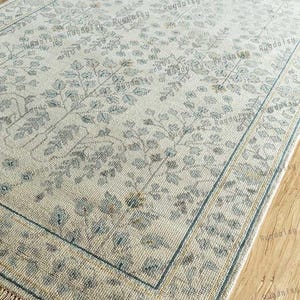 Könnte beinhalten: Ein hellblauer und beiger Teppich mit Blumenmuster und Fransen. Der Teppich hat einen dezenten Used-Look.