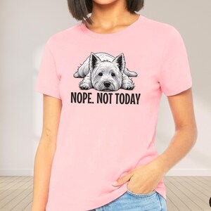 May include: A light pink t-shirt featuring a black and white illustration of a West Highland White Terrier dog lying down. The text "NOPE. NOT TODAY" is printed below the dog. The shirt is a solid color.