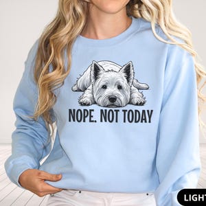 May include: Light blue sweatshirt featuring a graphic of a West Highland White Terrier dog lying down. The text "NOPE. NOT TODAY" is printed below the dog. The sweatshirt is a solid light blue color.