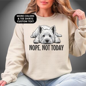 May include: Beige sweatshirt featuring a black and white illustration of a West Highland White Terrier dog. The text "NOPE. NOT TODAY" is below the dog. The top left corner has the text "MORE COLORS & TEE SHIRTS CUSTOM TEXT".