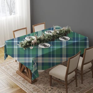 May include: A green and blue plaid tablecloth covers a wooden table set for a holiday meal. The table is decorated with a garland, plates, and decorative deer figurines. The chairs have beige upholstered seats.