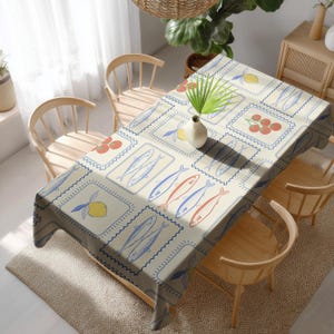 Könnte beinhalten: Rechteckige Tischdecke in Creme mit einem sich wiederholenden Muster aus Fischen, Zitronen und Tomaten in Blau, Rot und Gelb. Das Design ist von einem blauen, gezackten Rand umgeben. Die Tischdecke liegt auf einem Holztisch mit Holzstühlen.