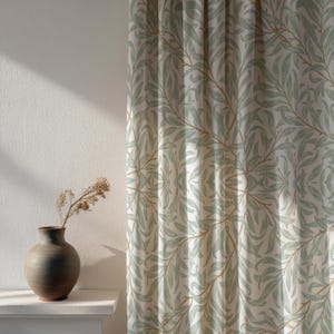 Può includere: Tende con un motivo ripetuto di foglie verdi e rami marroni su sfondo bianco. Un vaso marrone con fiori secchi è appoggiato su una mensola bianca. Le tende sono parzialmente tirate, la luce del sole illumina il muro.