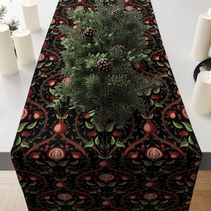 May include: A black table runner with a repeating pattern of pomegranates and leaves in red and green. The runner is decorated with a small evergreen arrangement and candles.