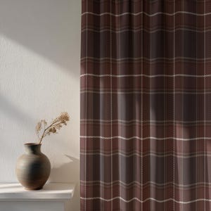 May include: Brown plaid curtain with white and beige accents. The curtain is hanging next to a white wall. A dark vase with dried flowers sits on a white shelf.