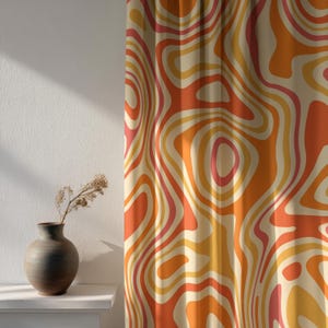 May include: Curtains with a retro design. The fabric has a swirling pattern in shades of orange, yellow, and pink against a cream background. A dark vase with dried flowers sits on a white shelf.