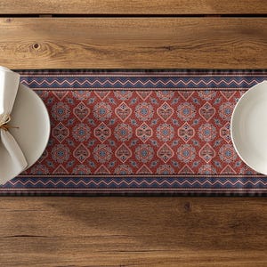 Puede incluir: Una mesa puesta con un camino de mesa estampado en rojo y azul, con platos y servilletas blancas. El camino de mesa tiene un diseño floral detallado. Las servilletas están atadas con hilo. Sobre una mesa de madera.