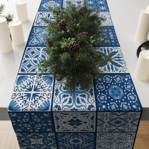 Peut inclure: Chemin de table à motifs bleus et blancs avec un motif de carreaux. Le chemin de table est orné d'une plante verte et de pommes de pin. Des bougies blanches sont sur la table.