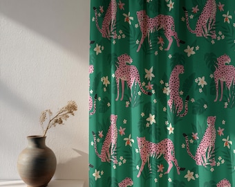 May include: Green curtain with a repeating pattern of pink cheetahs with black spots, white flowers, and green leaves. The cheetahs are in various poses. The curtain is hanging in front of a white wall with a vase and dried flowers.