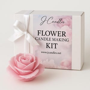 Puede incluir: Una vela rosa con forma de rosa junto a una caja blanca atada con una cinta blanca. La caja está etiquetada como "Flower Candle Making Kit" con el sitio web jcandles.net. La vela es de color rosa pálido.