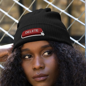 Może przedstawiać: Czarna czapka z czerwonym guzikiem, na którym widnieje napis "DELETE" w białym kolorze. Guzik ma białą strzałkę skierowaną w prawo.