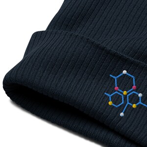 May include: A dark blue knitted beanie with a colorful embroidered chemical structure design.